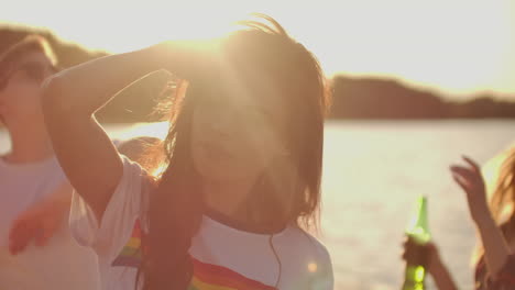 Young-girl-with-long-dark-hair-in-a-short-white-t-shirt-with-a-rainbow-is-dancing-on-the-beach-party-with-her-friends.-Her-hair-is-flying-on-the-wind.-She-enjoys-partytime-with-her-eyes-closed.